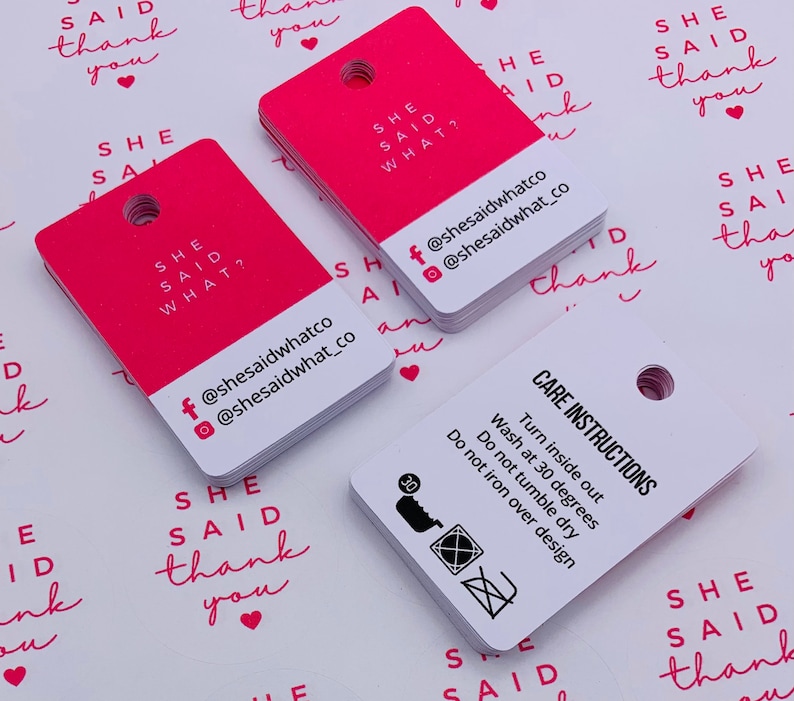 K&ouml;nnte beinhalten: Rosa quadratische H&auml;ngeetiketten mit dem Text "She Said What?" und Social-Media-Handles. Wei&szlig;e quadratische H&auml;ngeetiketten mit dem Text "Pflegehinweise" und Waschanweisungen.