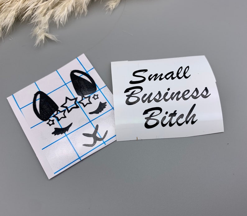 May include: Two white stickers, one with a black cartoon face with eyelashes and stars, and the other with the text "Small Business Bitch" in black cursive.