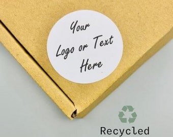 以下が含まれることがあります： 白い丸いステッカーに黒い文字で「Your Logo or Text Here」と印刷されています。ステッカーは茶色の段ボール箱に貼られています。箱の下の白い背景に黒い文字で「Recycled sticker paper」と印刷されています。
