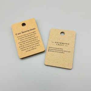 K&ouml;nnte beinhalten: Zwei braune Papieretiketten mit schwarzem Text. Das erste Etikett enth&auml;lt Pflegehinweise f&uuml;r Schmuck aus Polymer Clay. Das zweite Etikett tr&auml;gt den Text "The Drummond Craft Co." mit Kontaktinformationen.