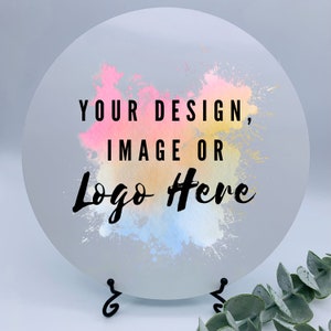 May include: A round, white, acrylic sign with a watercolor-style background in shades of pink, yellow, and blue. The text "YOUR DESIGN, IMAGE OR LOGO HERE" is written in black.