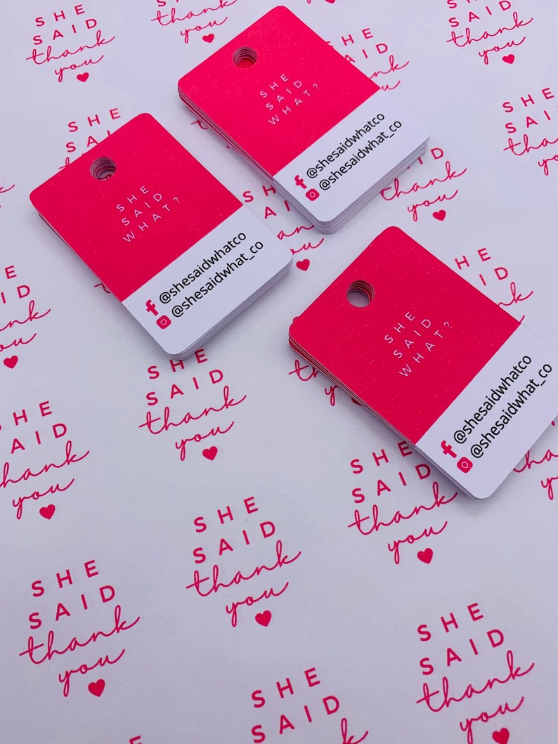 K&ouml;nnte beinhalten: Rosa und wei&szlig;e quadratische Etiketten mit dem Text "She Said" und "She Said What?" mit Social-Media-Handles f&uuml;r @shesaidwhatco. Die Etiketten haben ein Loch in der oberen Ecke.