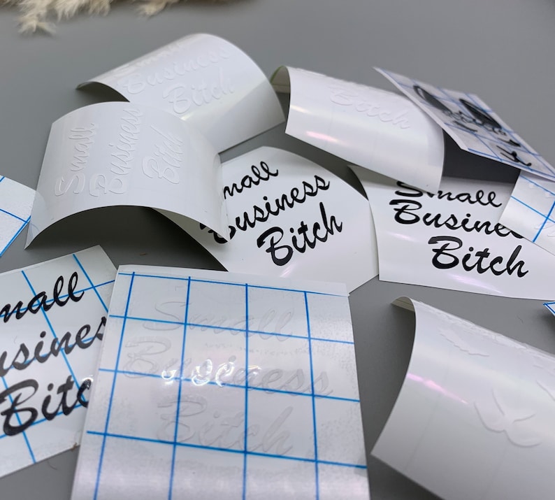 May include: White vinyl sheets with the text "Small Business Bitch" printed in black. The sheets are on a gray surface.