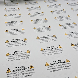 May include: A sheet of white warning labels with a yellow triangle and exclamation point. The labels read "Warning Choking Hazard Contains small parts. Please keep out of reach of children and pets. For decorative purpose only."
