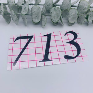 May include: Black vinyl sticker with the number 713 on a white background with a pink grid.