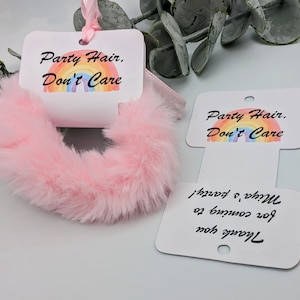 May include: A pink, fluffy scrunchie with a white tag that reads "Party Hair, Don't Care" above a rainbow graphic. A second tag says "Thank you for coming to Miya's party!"