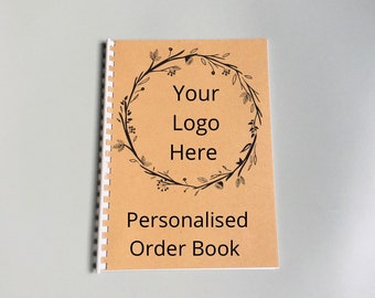 May include: A brown paper order book with a white spiral binding. The cover features a black floral wreath with the text "Your Logo Here" and the words "Personalised Order Book".