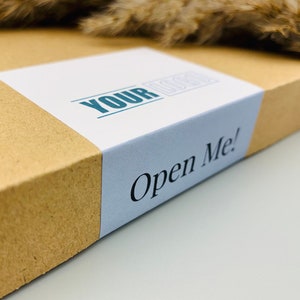 May include: A brown cardboard box with a white label that says "YOUR LOCAL" and a blue label that says "Open Me!"