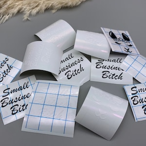 May include: A collection of white vinyl stickers with the text "Small Business Bitch" in black lettering. The stickers are on a white gridded backing.