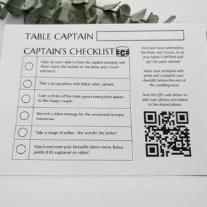 May include: A white rectangular card titled TABLE CAPTAIN with a CAPTAIN'S CHECKLIST. The checklist includes six tasks with circular checkboxes, instructions for the table captain, and a QR code for uploading photos and videos to a shared album.