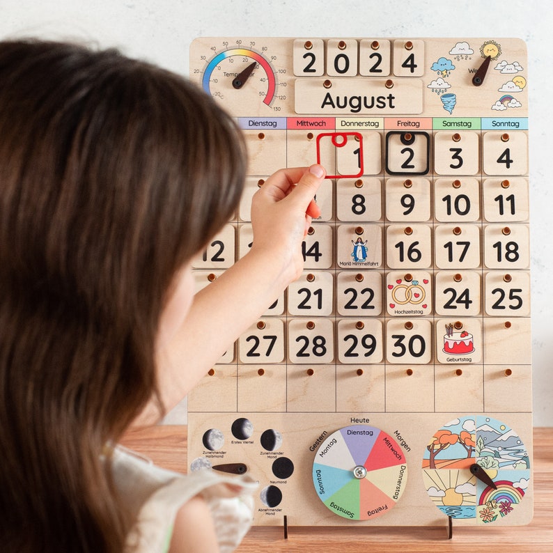 A wooden calendar with a white background and black numbers. The calendar is for August 2024 and includes a thermometer, weather icons, and small illustrations for special days. The calendar is mounted on a stand with a moon phase chart, a weather wheel, and a seasonal scene.
