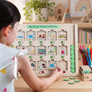 Puede incluir: Un tablero de tareas de madera clara titulado My Daily Responsibilities con filas de azulejos cuadrados que presentan ilustraciones coloridas de tareas como ducharse, cepillarse los dientes y hacer la tarea. Cada azulejo tiene un interruptor deslizante.