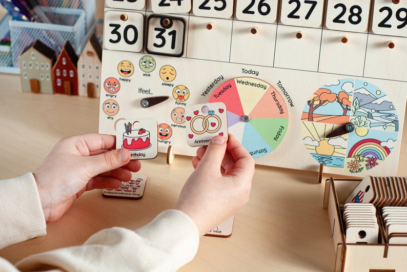 May include: A wooden calendar with a daily calendar, a wheel for days of the week, a weather wheel, and a set of emotion and event cards. The cards include images of a birthday cake, wedding rings, and various emotions.
