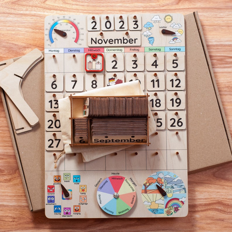 May include: Wooden calendar with a brown wooden frame and a white background. The calendar is for November 2023 and has a small wooden box with the word "September" on it. The calendar also has a small wooden wheel with different days of the week and a small wooden wheel with different weather icons.