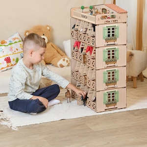 May include: A four-storey wooden toy horse stable with individual stalls, green shuttered windows, and a top-level balcony. The structure features the word RANCH printed on the front. It includes small plastic horse figurines and miniature figures.