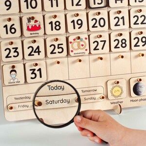 May include: Wooden perpetual calendar with numbered days and illustrated event markers. Features a magnifying glass focused on "Saturday". Includes weather and moon phase indicators. A fun and educational tool for children.