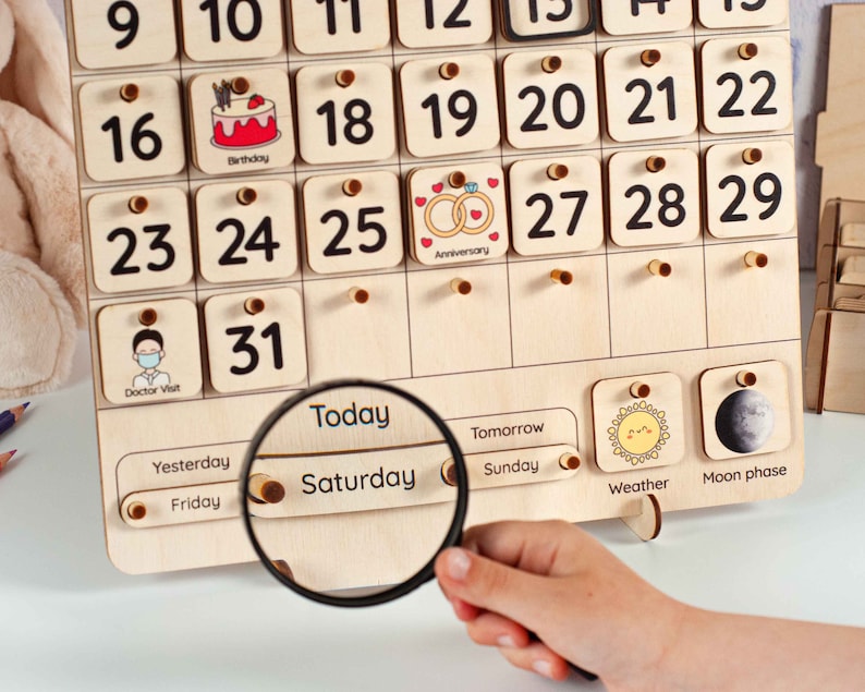 May include: Wooden perpetual calendar with numbered days and illustrated event markers. Features a magnifying glass focused on "Saturday". Includes weather and moon phase indicators. A fun and educational tool for children.
