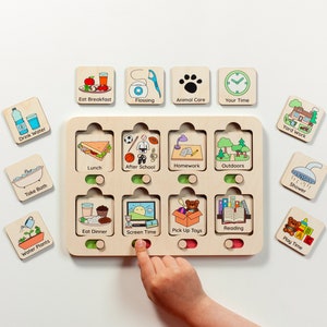 Puede incluir: Un tablero de tareas de madera con ocho ranuras que contienen fichas cuadradas extra&iacute;bles. Cada ficha presenta una ilustraci&oacute;n colorida y texto para tareas diarias como Eat Breakfast, Flossing, Animal Care, Your Time, Drink Water, Take Bath, Water Plants, Lunch, After School, Homework, Outdoors, Eat Dinner, Screen Time, Pick Up Toys, Reading, Yard Work, Shower y Play Time.