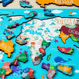 May include: A colorful wooden world map puzzle with names of countries and continents. The puzzle pieces are shaped like the continents and are arranged on a blue background. The puzzle is made of wood and has a light brown finish.