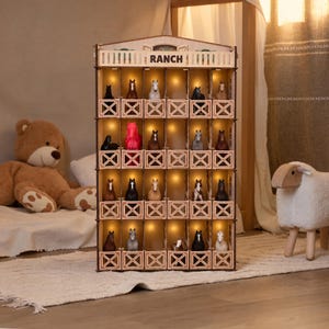 May include: A wooden multi-level display shelf with the word RANCH printed on the top facade. The structure features twenty individual stalls, each illuminated by a warm light, housing various miniature horse figurines in diverse colours and poses.