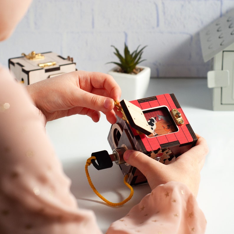 May include: A child opens a wooden box with a red door and a keyhole. The box has a picture of a dog and a cat inside. The box is made of wood and has a brown and black finish.