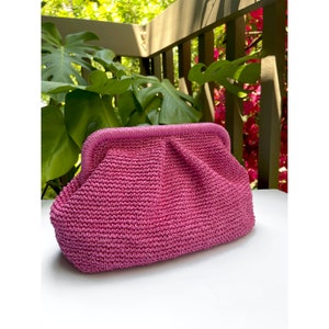 Puede incluir: Un bolso de mano tejido de color rosa con un dise&ntilde;o fruncido. El bolso tiene un cierre de broche met&aacute;lico.