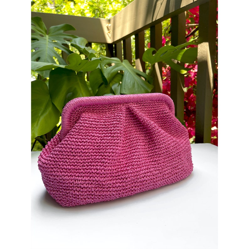Puede incluir: Un bolso de mano tejido de color rosa con un dise&ntilde;o fruncido. El bolso tiene un cierre de broche met&aacute;lico.