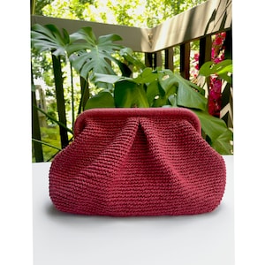Puede incluir: Un bolso de mano de crochet rojo con forma redondeada y cierre de broche.