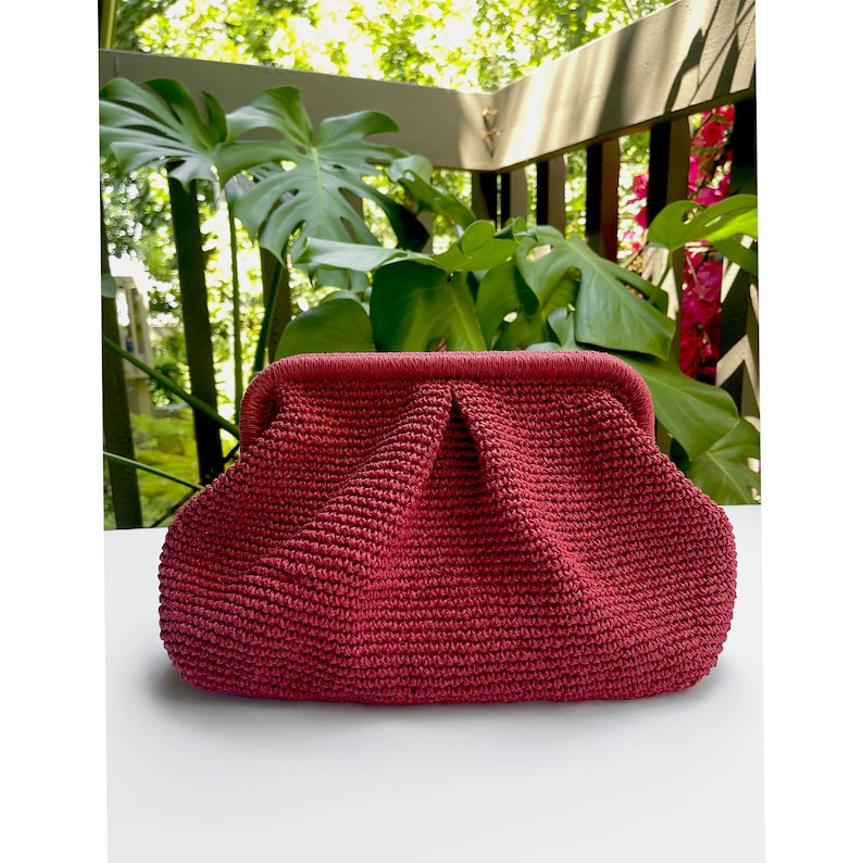 Puede incluir: Un bolso de mano de crochet rojo con forma redondeada y cierre de broche.