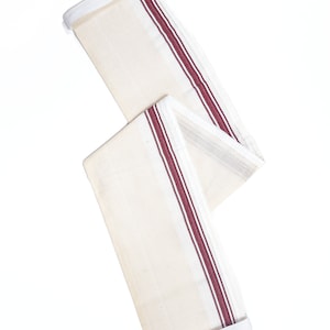 May include: A white cotton fabric with two red stripes running down the length of the fabric. The fabric is folded in half and has a white trim on the edges.