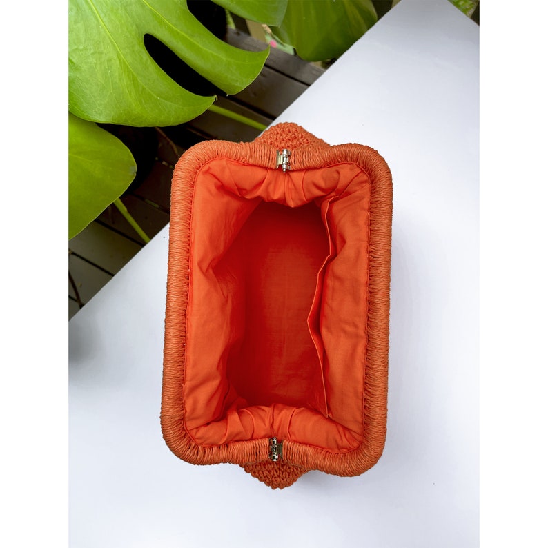 Puede incluir: Clutch tejido naranja con cierre de cremallera y forro de tela naranja brillante.