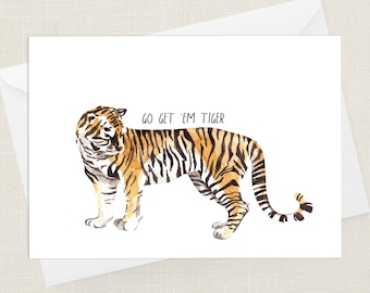 May include: A watercolor illustration of a tiger with orange and black stripes. The tiger is standing on a white background with the text "GO GET 'EM TIGER" above it.