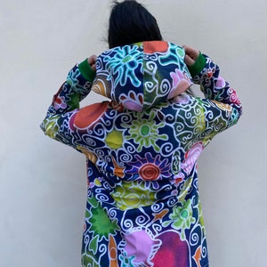 May include: A colourful hooded jacket with a swirling, abstract pattern in shades of blue, green, orange, pink, and yellow. The jacket has a zip closure and a drawstring hood.