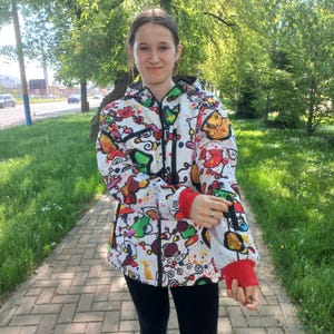 May include: A white hooded jacket with a colorful abstract print. The jacket has a zipper closure and red accents on the cuffs.