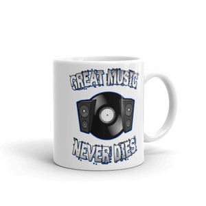 May include: White ceramic mug featuring a black vinyl record and two speakers. The text "GREAT MUSIC NEVER DIES" is printed in a blue and white design. The mug has a white handle and a glossy finish.