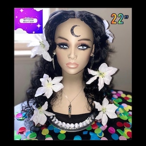 Puede incluir: Una cabeza de maniquí con cabello largo y negro ondulado, adornada con flores blancas. La cara tiene un tatuaje de media luna y lleva un collar. El cabello mide 55,88 cm. El texto "BESTYLEZZ16 BEAUTY SHOP" es visible.