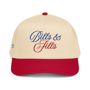 May include: Cream-colored baseball cap with a red brim and button. The cap features the embroidered text "Bills & Fills" in blue and red script. A small embroidered design is on the side.