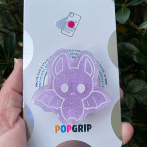 May include: Purple glitter bat phone grip with the text "PopGrip" and "L Twice to Grip, Tirez-le De!" on the packaging.