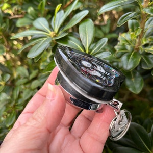 May include: A black and silver keychain with a heart-shaped charm. The charm has a glittery black surface with colorful glitter accents. The keychain has a silver ring and a silver hook.