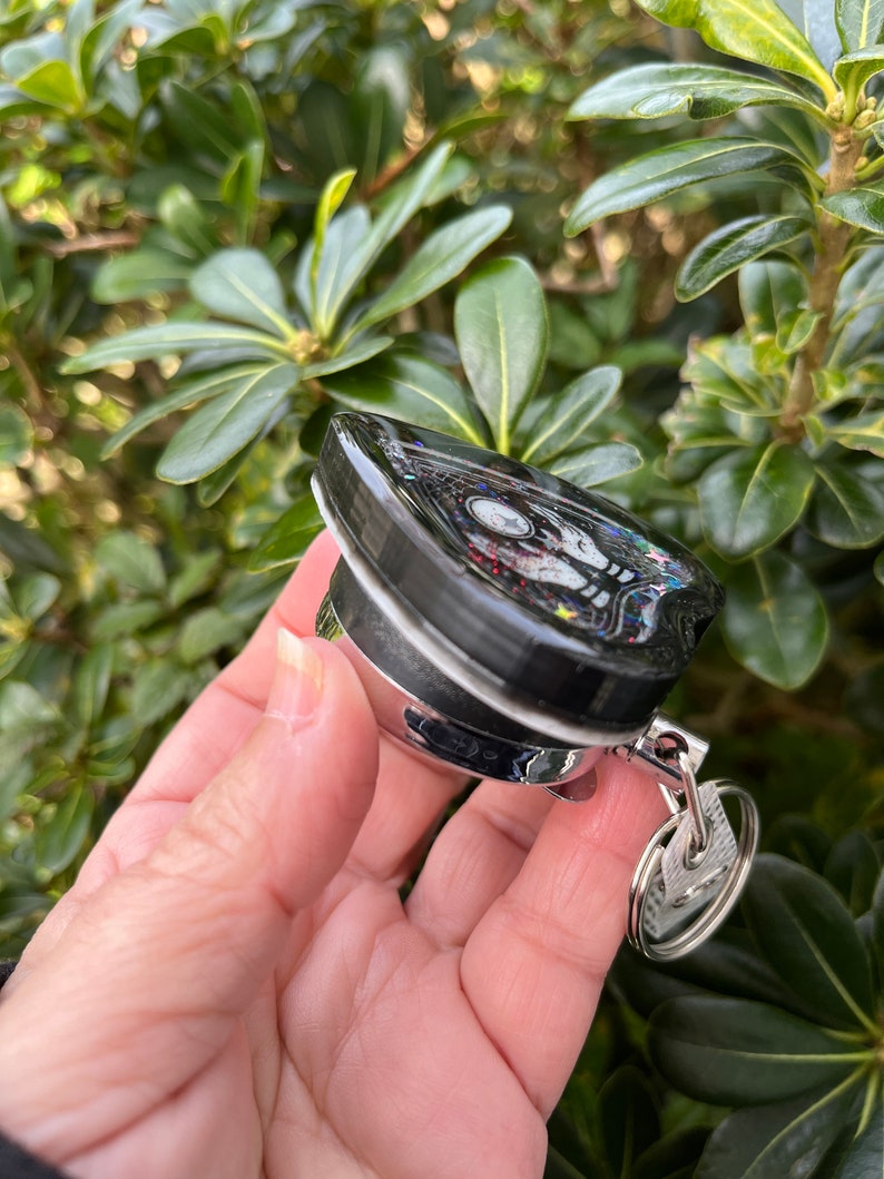 May include: A black and silver keychain with a heart-shaped charm. The charm has a glittery black surface with colorful glitter accents. The keychain has a silver ring and a silver hook.