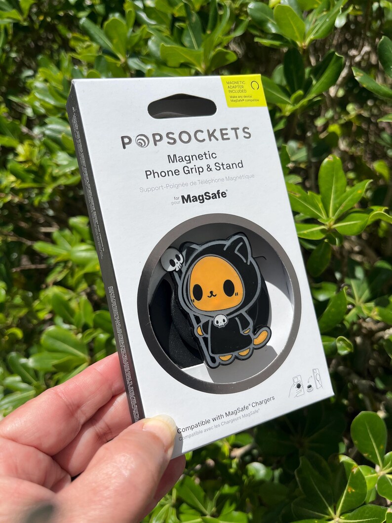 May include: A white box with a black and orange cartoon character PopSocket phone grip and stand. The box reads "POPSOCKETS Magnetic Phone Grip & Stand for MagSafe". The PopSocket has a black background.