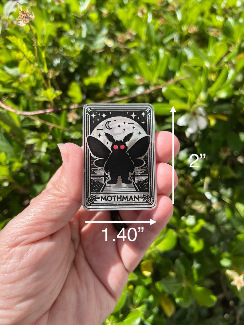 Puede incluir: Una pegatina de acr&iacute;lico transparente con una ilustraci&oacute;n en blanco y negro de Mothman, una criatura con alas grandes y ojos rojos. La pegatina mide 5 cm de alto y 3,5 cm de ancho. La pegatina tiene un fondo blanco con estrellas negras y una luna creciente.