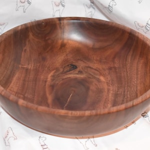 Puede incluir: Un tazón grande de madera marrón oscuro con un acabado liso y pulido. El tazón está hecho de madera de nogal y tiene un patrón de veta natural.