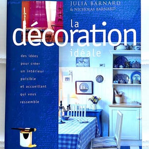 Peut inclure: Un livre intitulé "la décoration idéale" de Julia Barnard & Nicholas Barnard. La couverture présente une nappe à carreaux bleus et blancs sur une table à manger avec des chaises blanches. La couverture du livre est bleue avec du texte blanc.