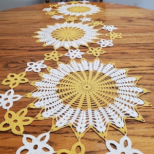 Completed doily made from pattern, in yellow and white. Image shows three large starburst-type doilies with 2" flowers attached, winding in between the three large doilies.