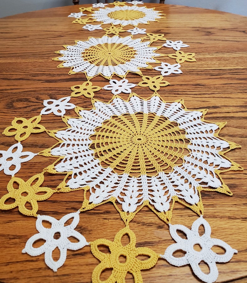 Completed doily made from pattern, in yellow and white. Image shows three large starburst-type doilies with 2" flowers attached, winding in between the three large doilies.