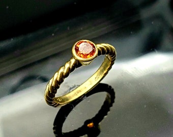 May include: A gold ring with a twisted band and a small, round, orange gemstone.