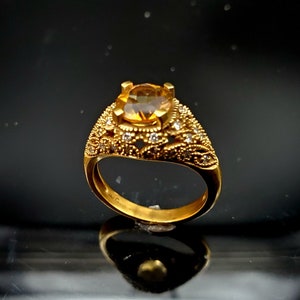 May include: A gold ring with a large, round, yellow gemstone surrounded by smaller, white gemstones. The ring has a delicate, ornate design.