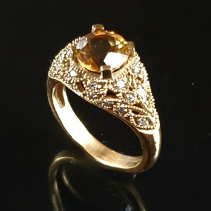 May include: A gold ring with a large, round, brown gemstone surrounded by smaller, clear gemstones. The ring has a delicate, intricate design.