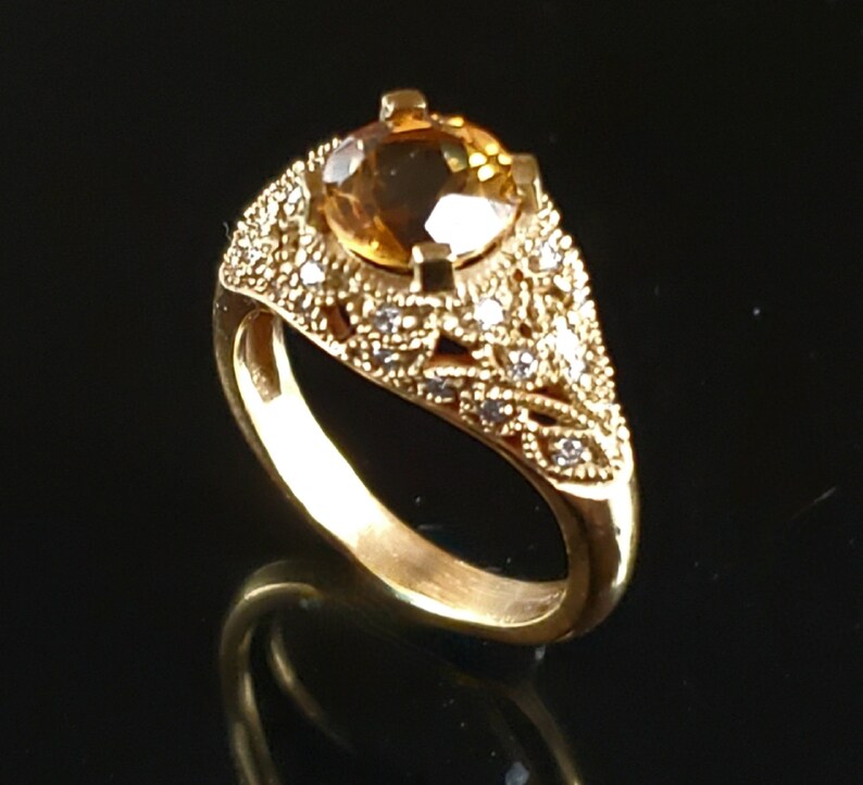 May include: A gold ring with a large, round, brown gemstone surrounded by smaller, clear gemstones. The ring has a delicate, intricate design.